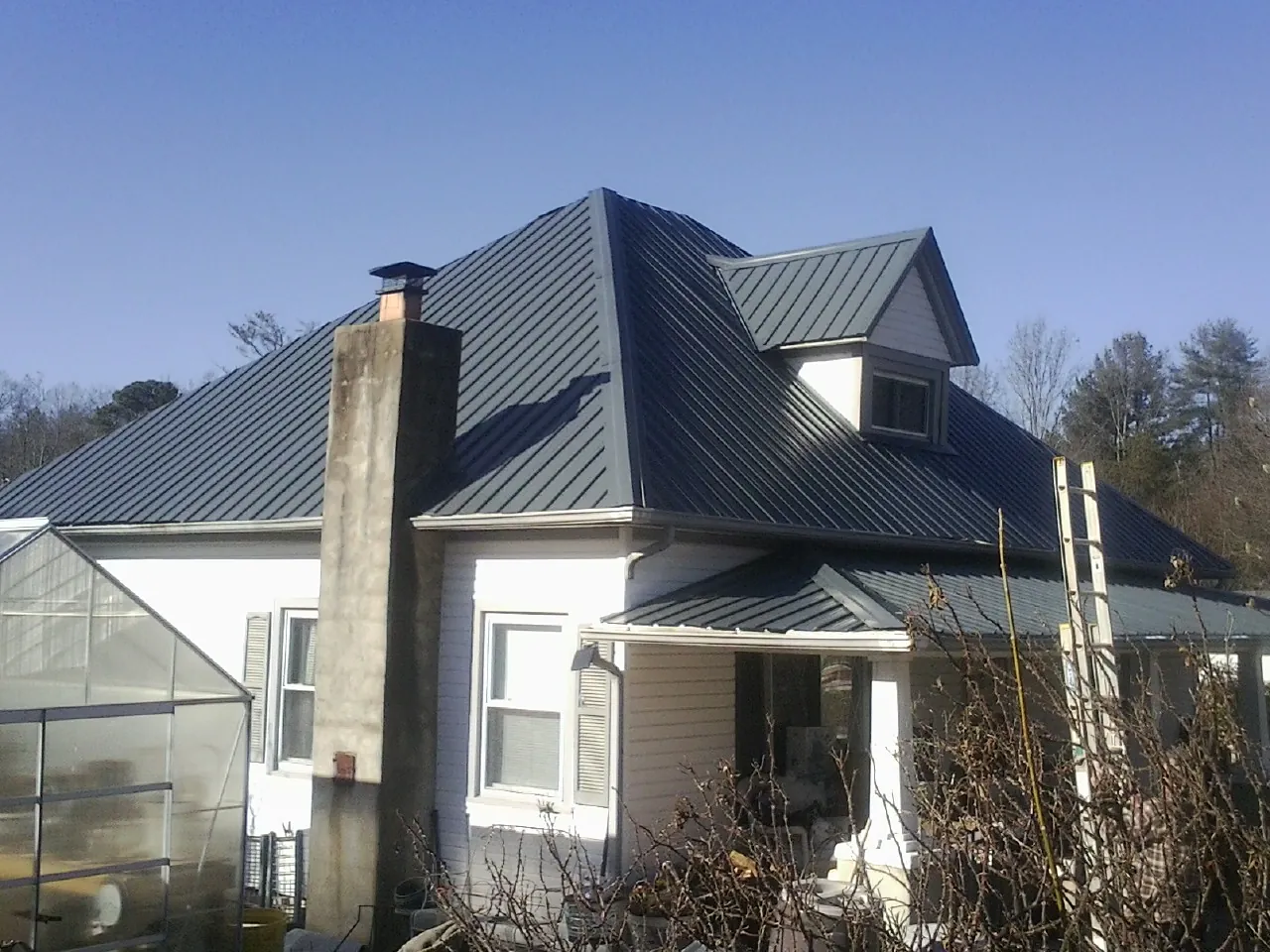 Dark blue standing seam metal roof on a white farmhouse with dormer — Slate & Tile Roof Repair by Roofing Brothers in Collins