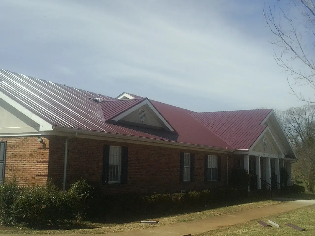 Red metal roof with gabled entries on a long brick building, from a Hail Damage Roof Repair job in Collins