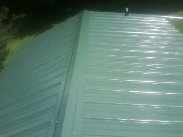 New green metal panels meeting at the ridge of a roof — Flat Roof Repair work by our crew in Collins